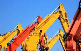 Untitled design 1446 | McCormick Insurance Close up of several bright excavator arms in yellow and red raised against a clear blue sky